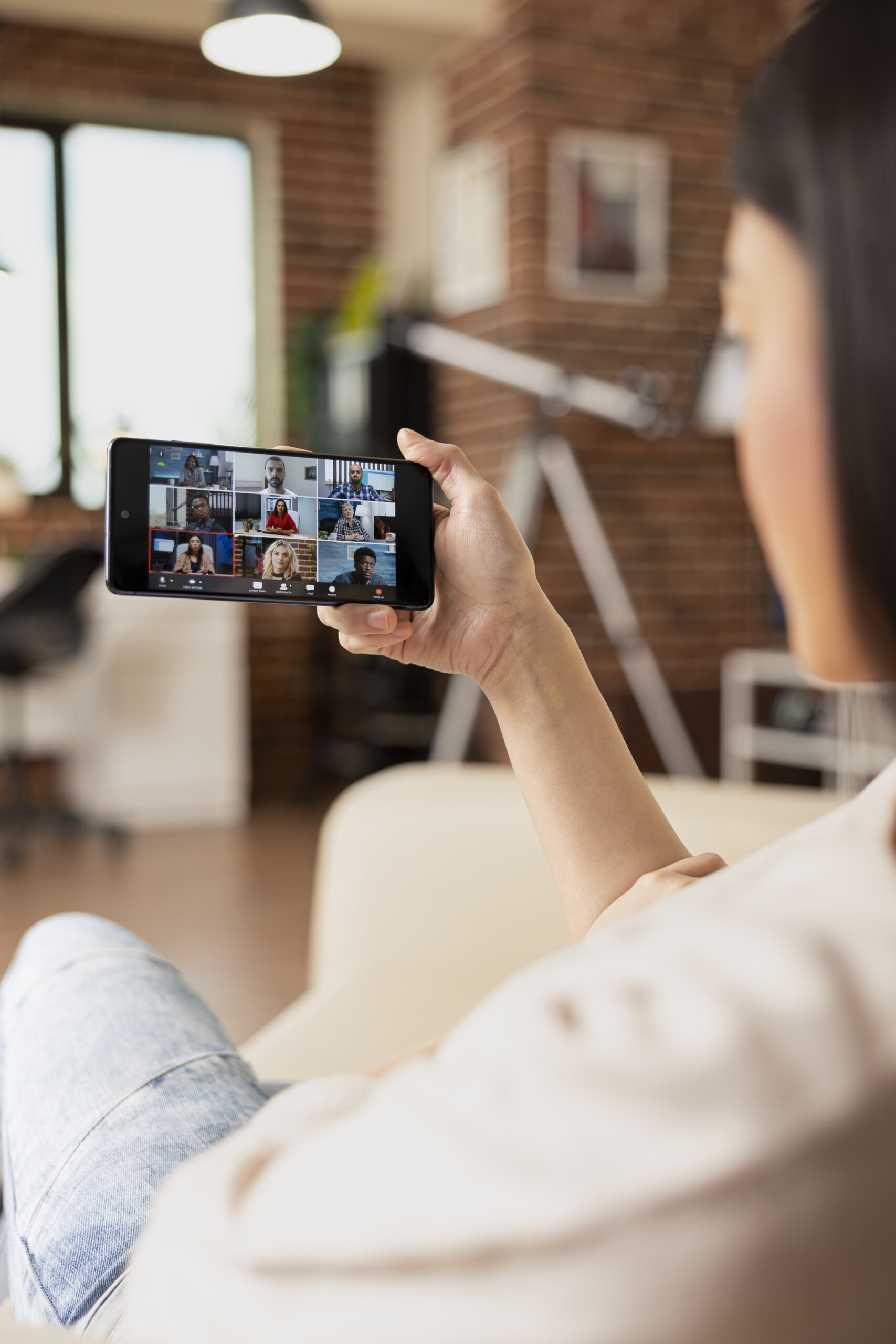 Female remote worker joining group video call on cellphone, collaborating with multiracial team during office briefing. Self employed woman participating in virtual shareholders meeting.
